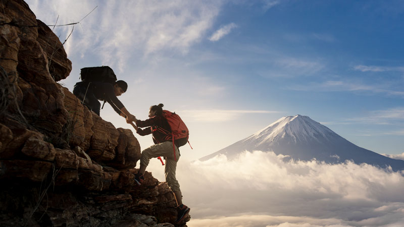 Man and woman rock climbing, helping each other with a snowy mountain in the background