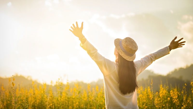 Women with arms outstretched to the sun, standing in a field of yellow flowers